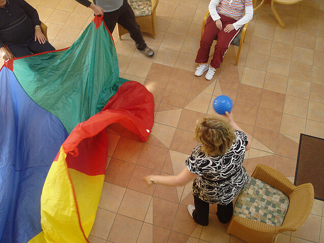 Menschen in Bewegung, sitzend und stehend, mit Ball und Plane