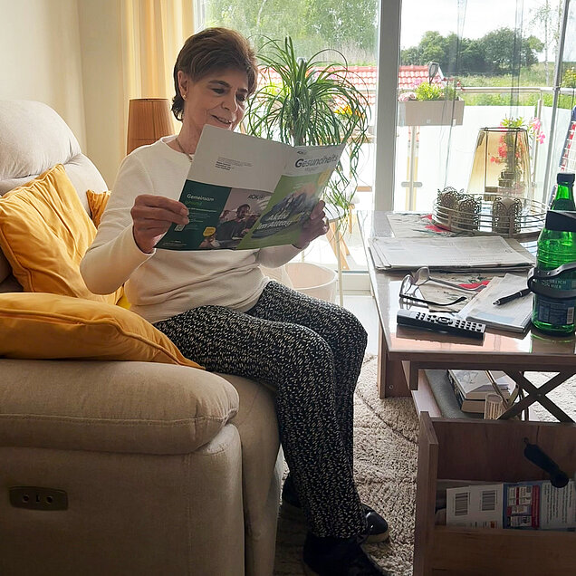 Eine Frau sitzt auf dem Sofa in Ihrem Wohnzimmer und liest einen Prospekt