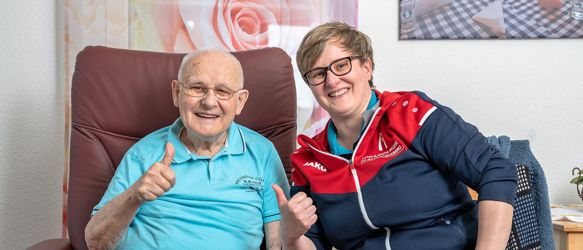 Betreutes Wohnen: Selbstbestimmt, aktiv und sicher im Alter. Mann und Pflegerin lächeln in die Kamera und halten die Daumen hoch.